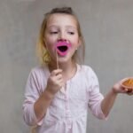 a little girl holding a donut and sticking a pink tongue out